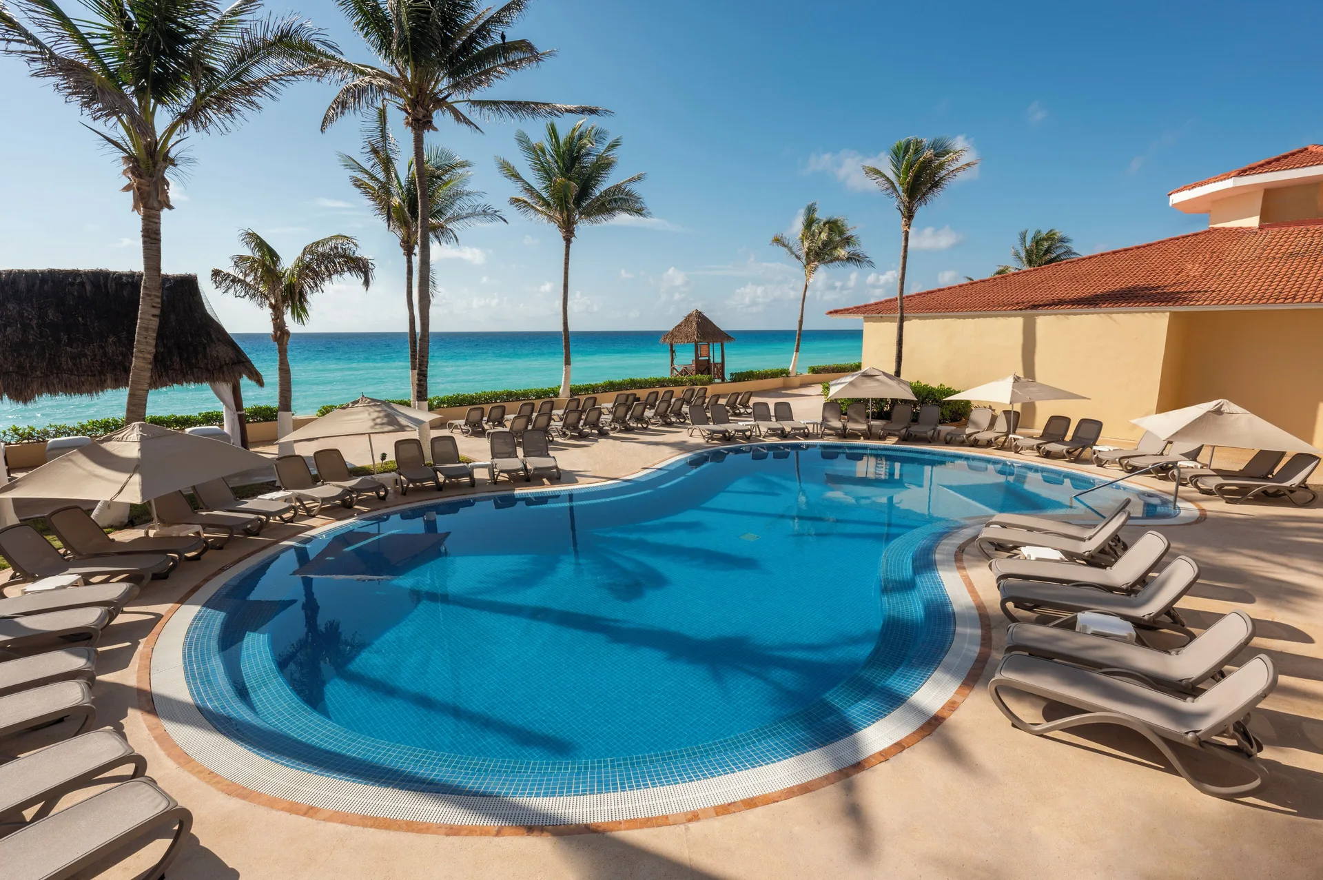 Oceanfront pool with loungers and palm trees at GR Solaris Cancun & Spa.