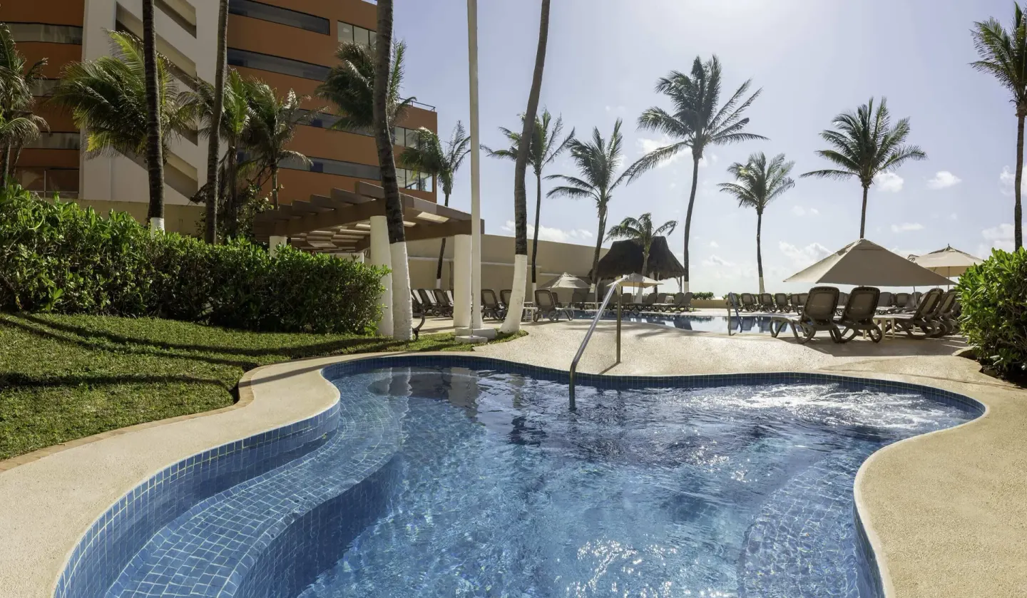 Palm-lined pool and sun loungers beside the resort building at GR Solaris Cancun & Spa.
