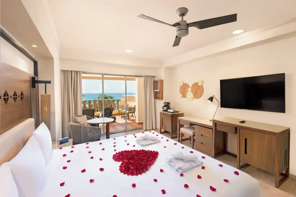 King bed with rose petals, balcony, TV, and ocean view at GR Solaris Cancun & Spa.