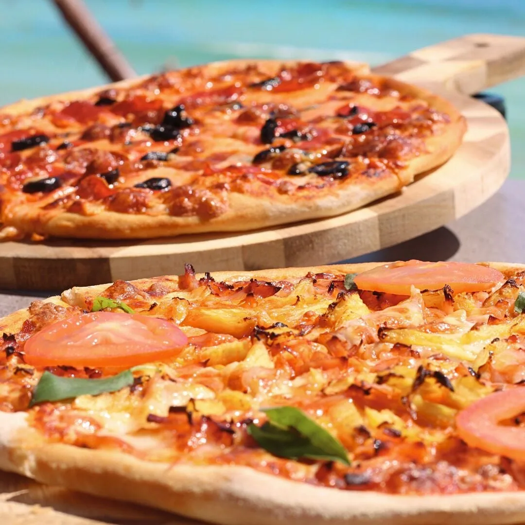 Two pizzas on wooden boards beside blue water at GR Solaris Cancun & Spa.