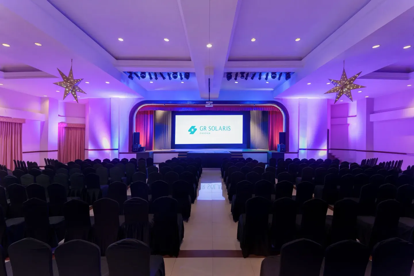 Rows of chairs face a lit stage in the event hall at GR Solaris Cancun & Spa.