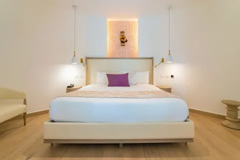 White king bed with purple accent pillow in a guest room at Grand Bavaro Princess.