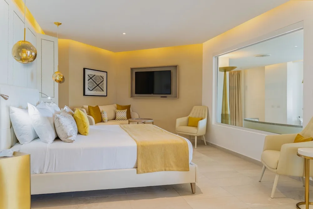 King bed with yellow accents and seating area in a guest room at Grand Bavaro Princess.
