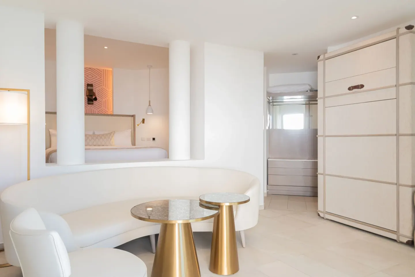 Guest room lounge with curved sofa, small tables, closet, and bed alcove at Grand Bavaro Princess.