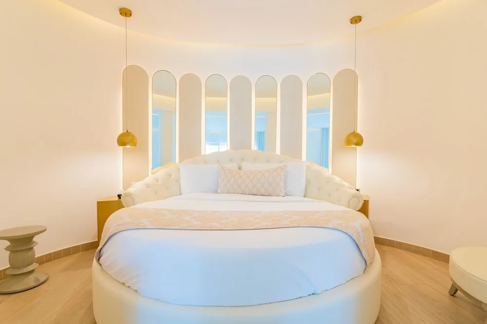 Round bed with arched mirror headboard and gold pendant lights at Grand Bavaro Princess.