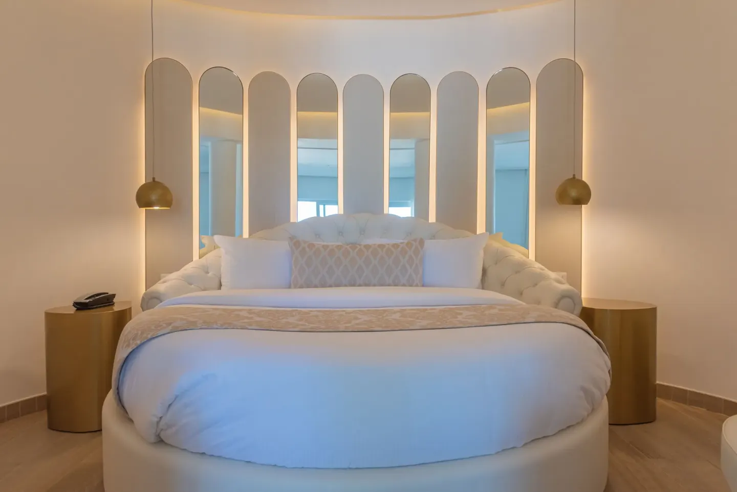 Round bed with mirrored headboard panels and gold pendant lights at Grand Bavaro Princess.
