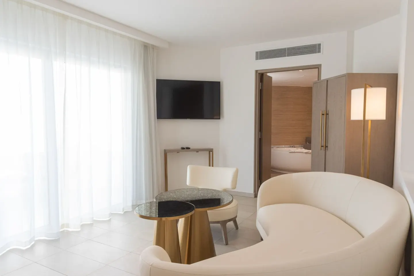 Guest room sitting area with curved sofa, TV, table, and bathroom doorway at Grand Bavaro Princess.
