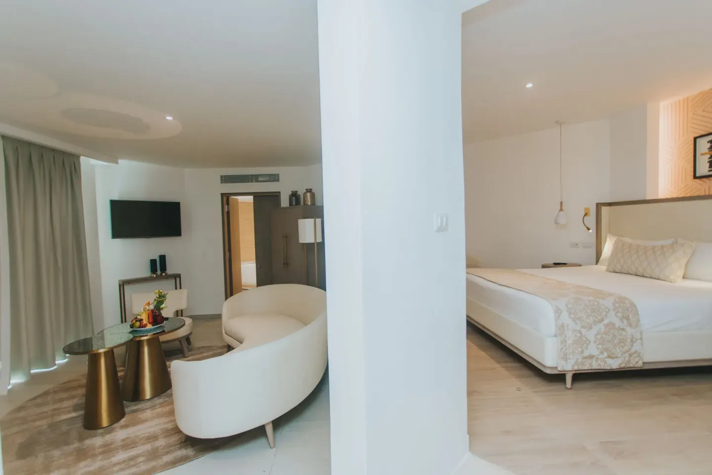 Guest suite with king bed, lounge seating, TV, and fruit plate at Grand Bavaro Princess.