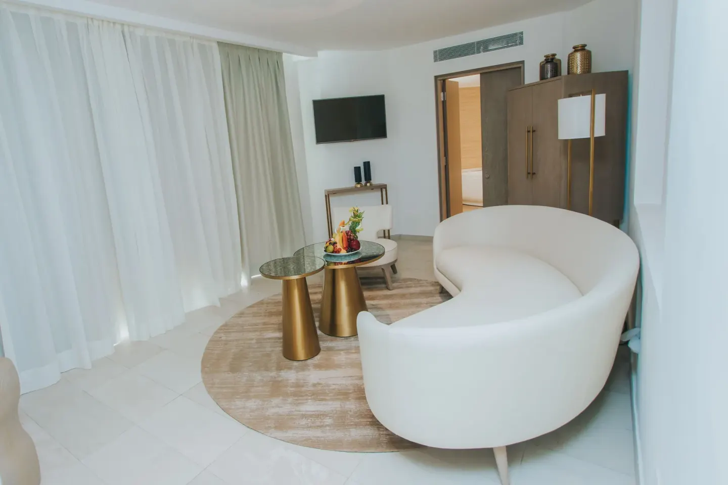Curved white sofa and curtained windows in a suite at Grand Bavaro Princess.