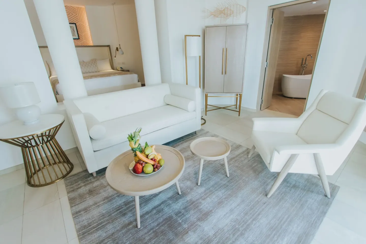Bungalow lounge with white sofa, fruit tray, and bathroom doorway at Grand Bavaro Princess.