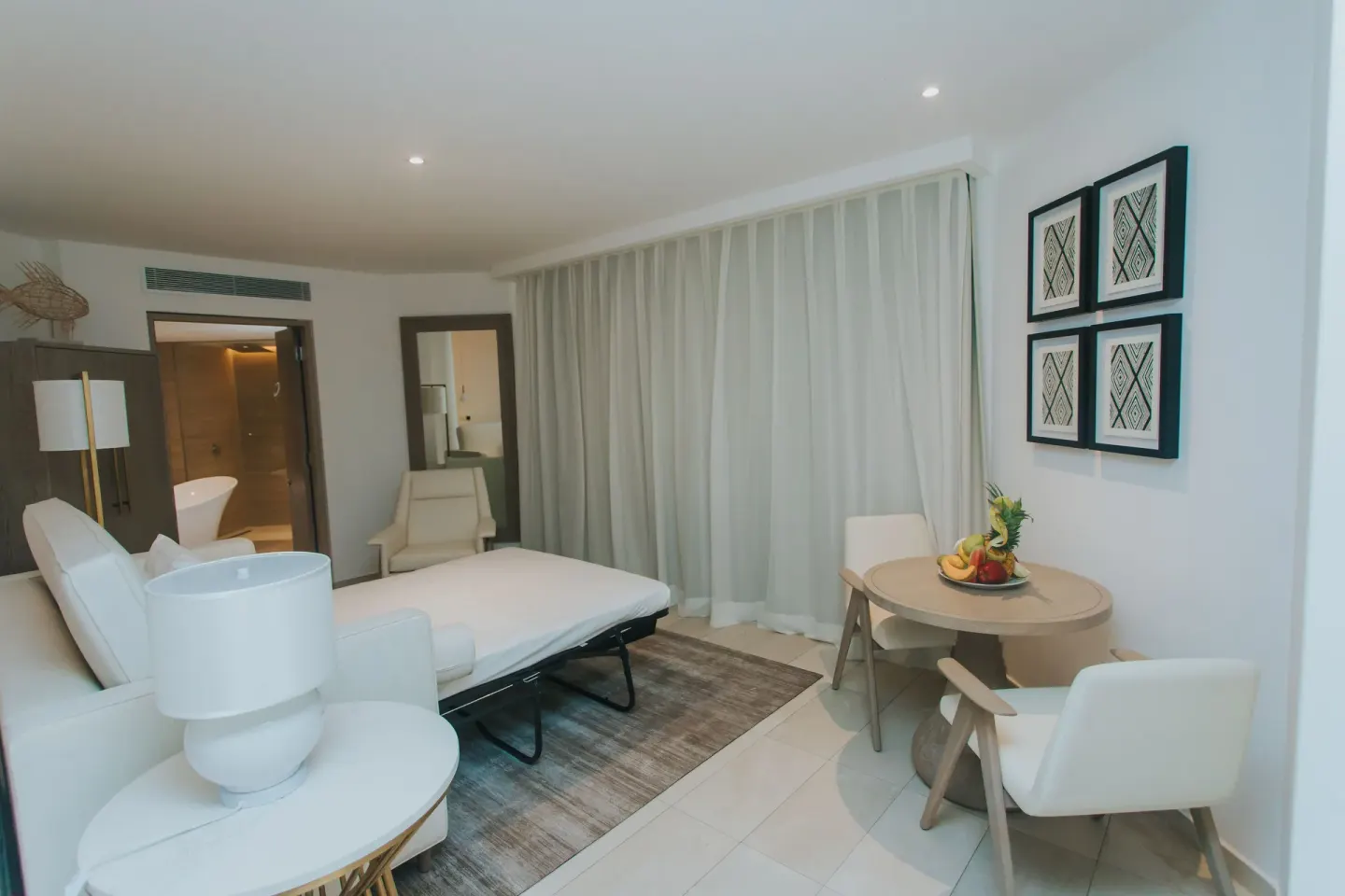 Bungalow room lounge with sofa bed, dining table, and curtains at Grand Bavaro Princess.