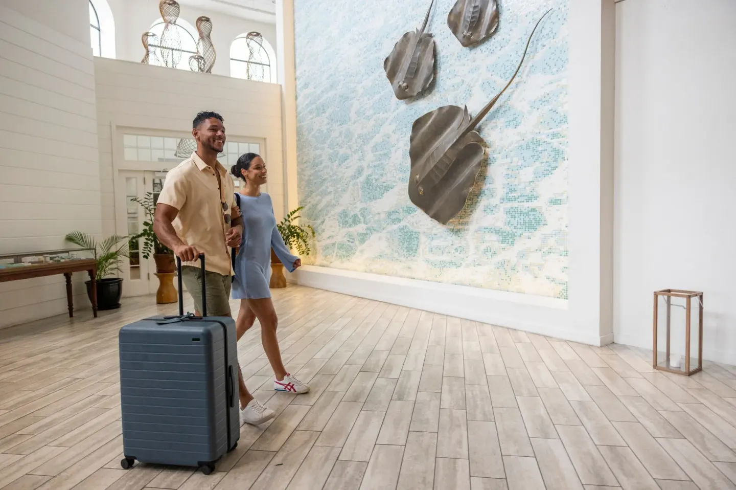 Guests with luggage pass a stingray wall artwork in the lobby at Grand Cayman Marriott Resort.