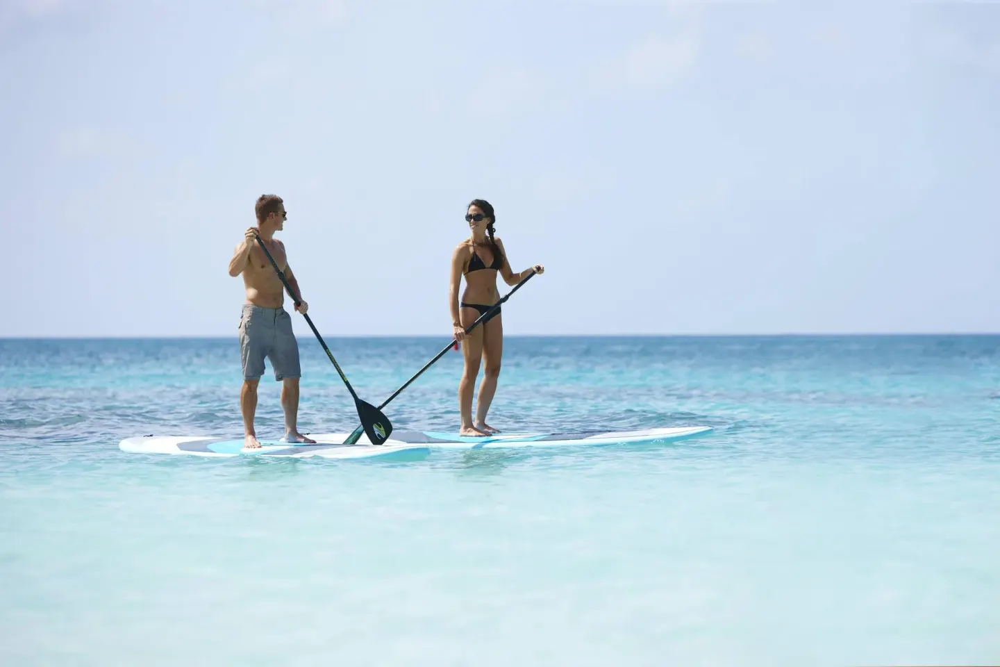 Two people paddleboarding on clear blue water near Grand Cayman Marriott Resort.
