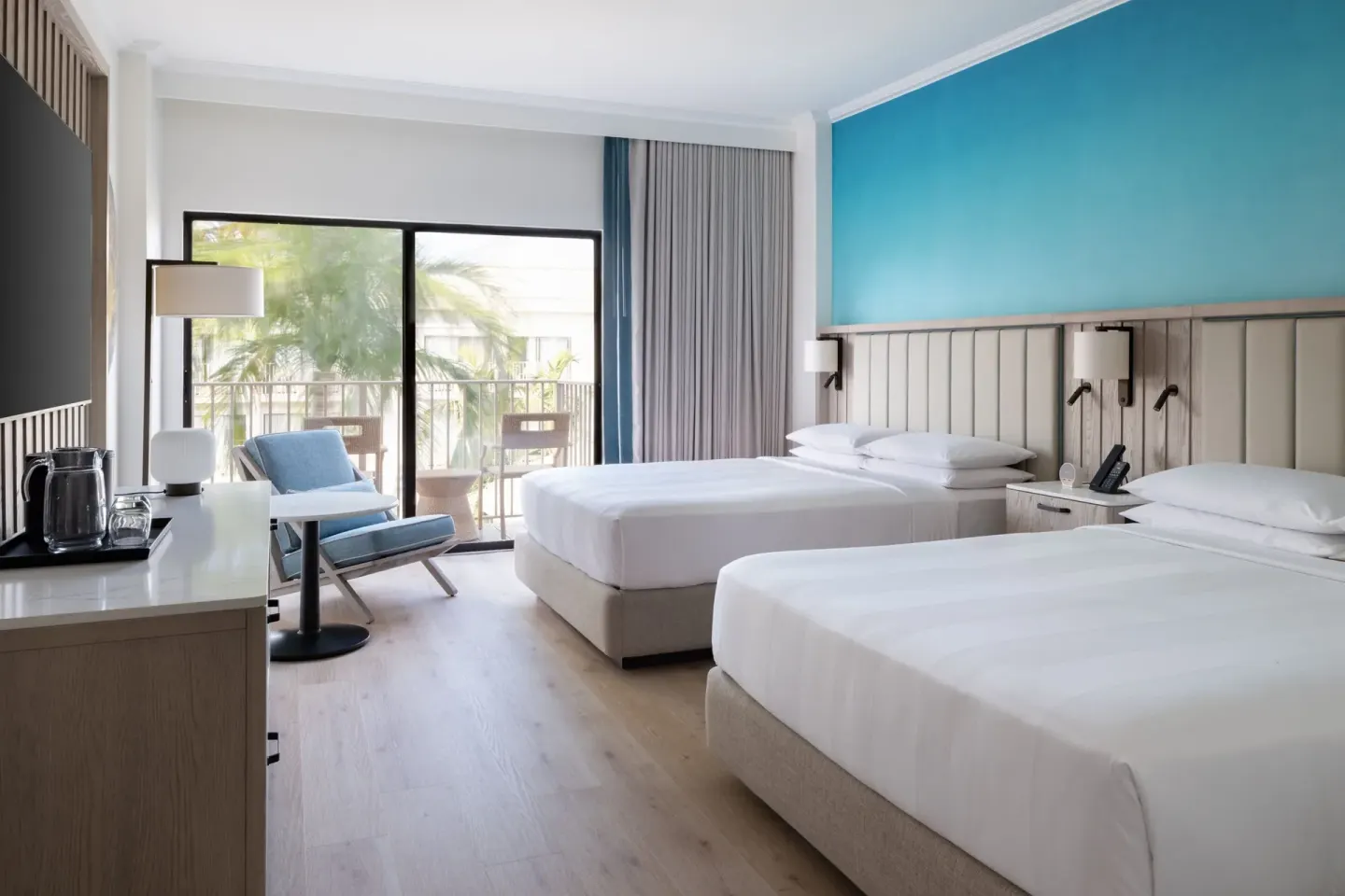 Two queen beds and a balcony seating area in a guest room at Grand Cayman Marriott Resort.