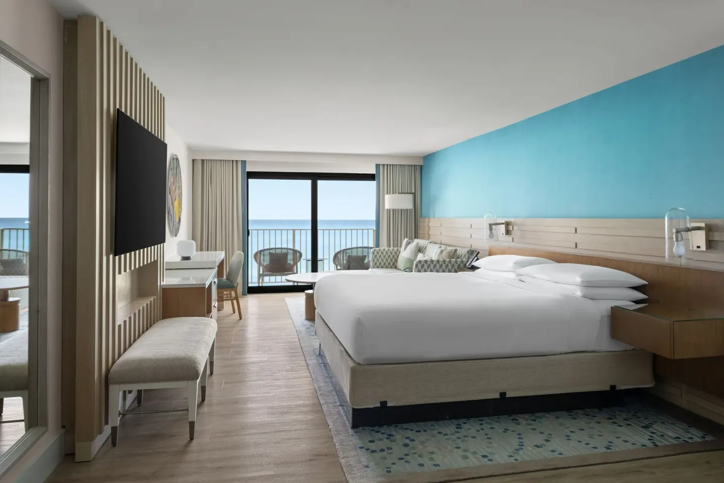 Room with king bed, sofa area, desk and ocean-facing balcony at Grand Cayman Marriott Resort.