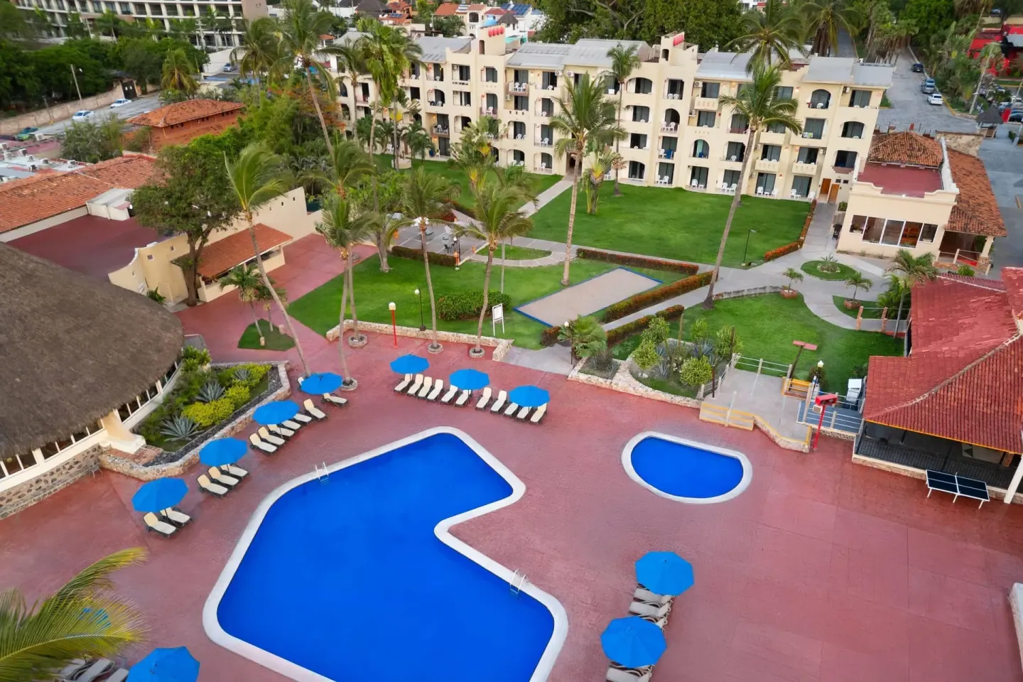 Aerial view of a pool courtyard, lawns, palms, and guest buildings at Grand Decameron Complex Bucerias.