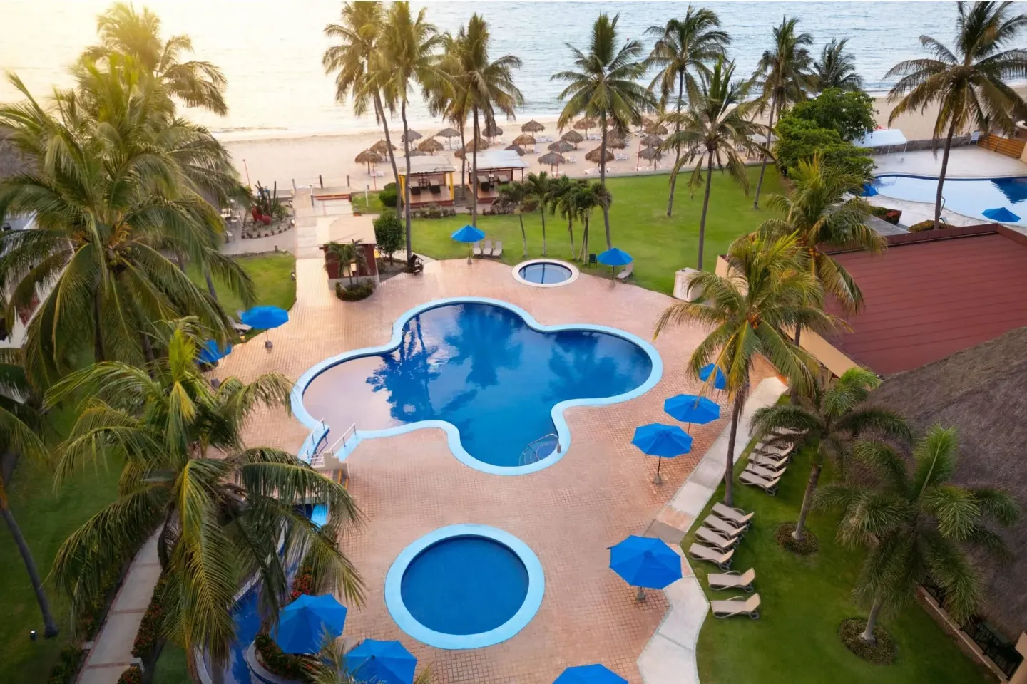 Aerial pool garden beside the beach with palms and blue umbrellas at Grand Decameron Complex Bucerias.