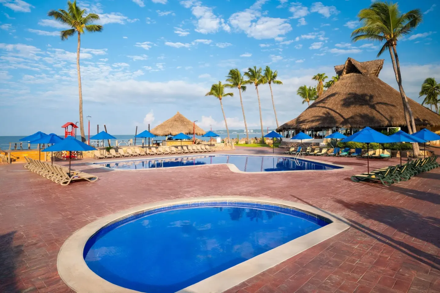 Beachfront pool area with palms, blue umbrellas, and ocean beyond at Grand Decameron Complex Bucerias.