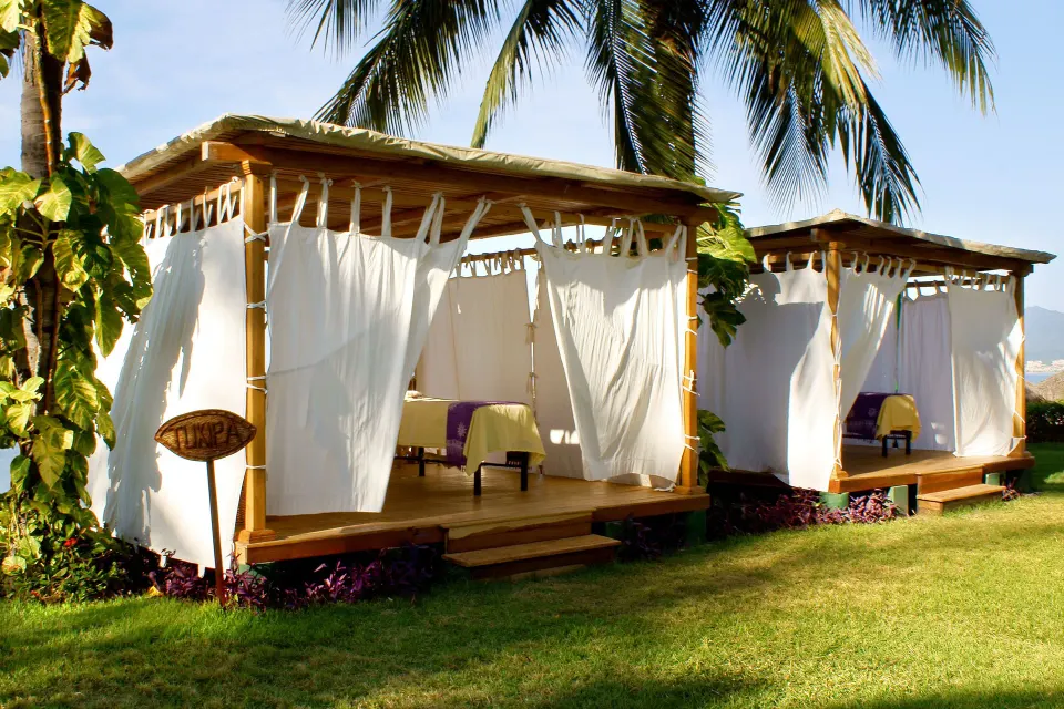 Beachside spa cabanas with white curtains and palm trees at Grand Decameron Complex Bucerias.