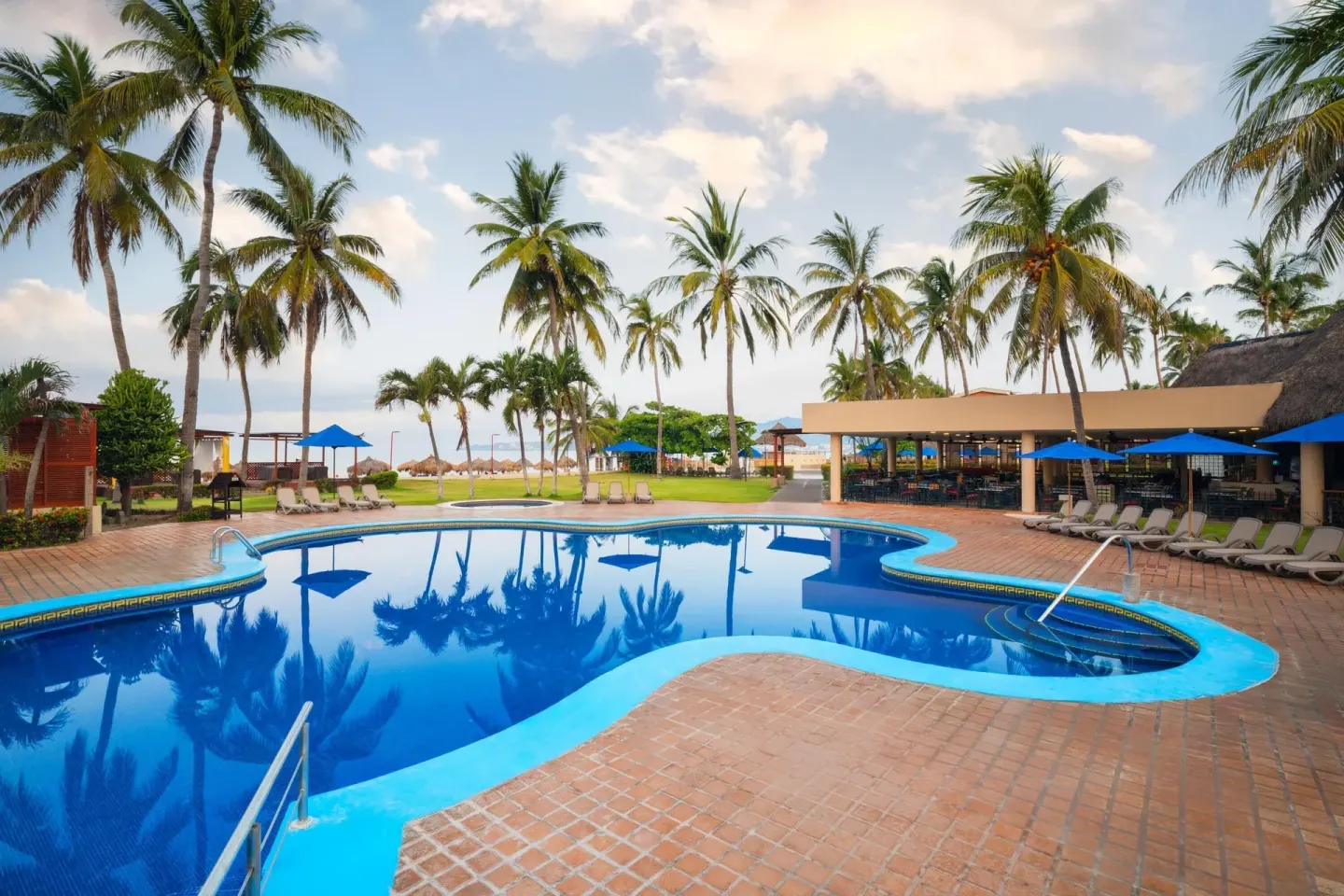 Curved pool near palms, loungers, and ocean at Grand Decameron Complex Bucerias.