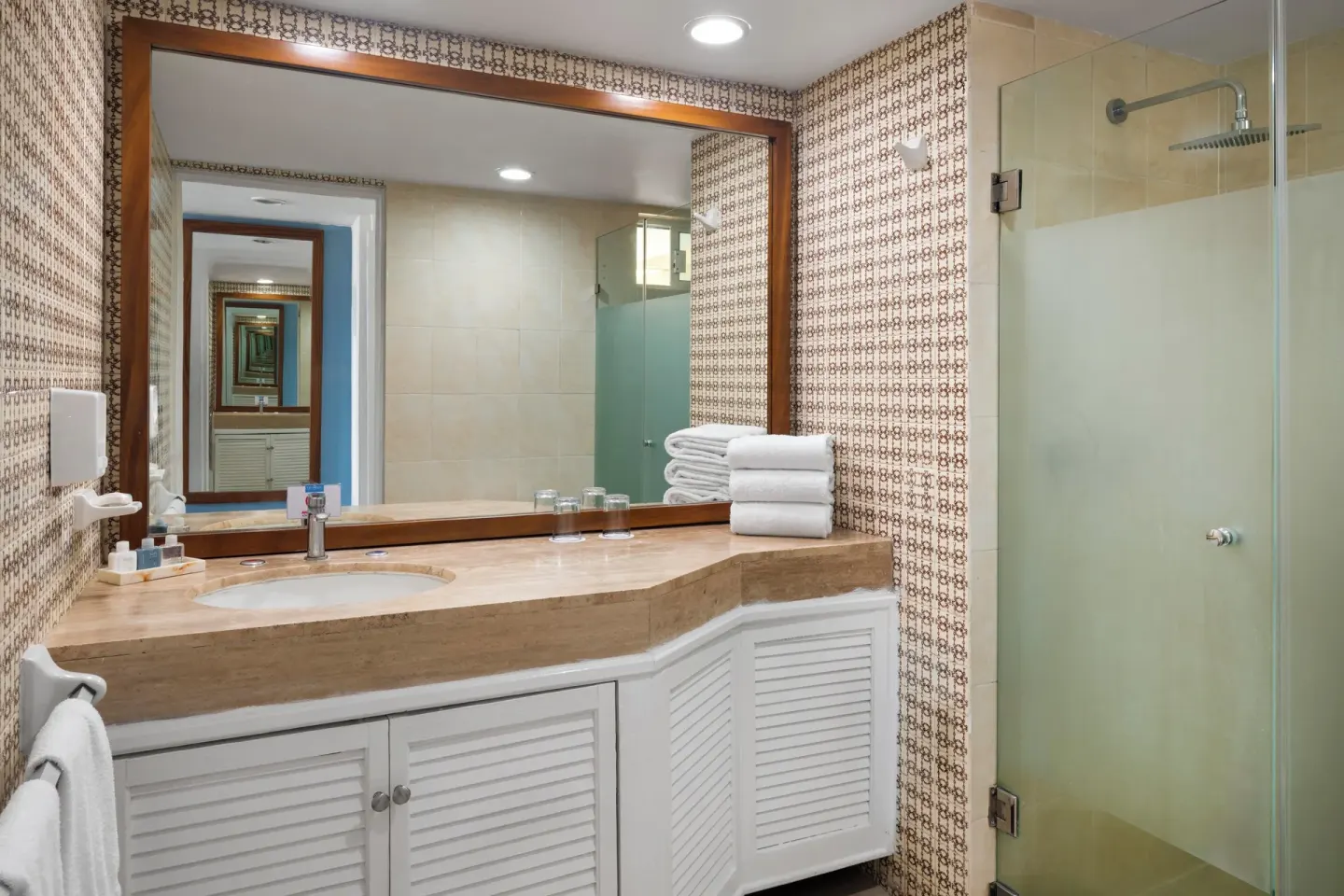 Bathroom with wide mirror, stone vanity and glass shower at Grand Decameron Complex Bucerias.