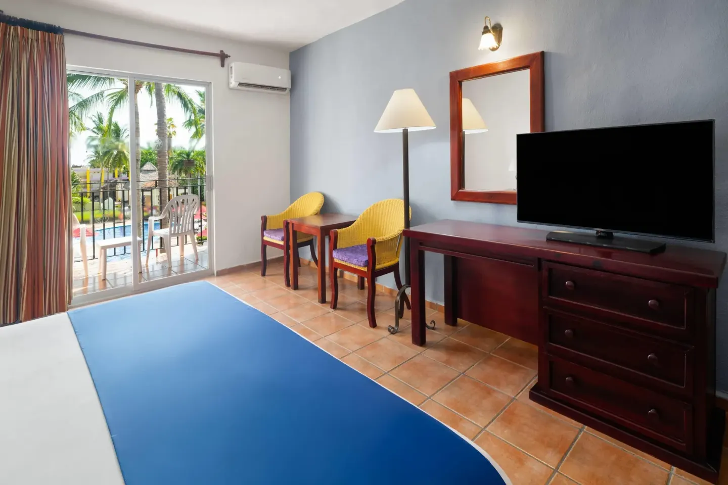 Guest room with TV, yellow chairs, and balcony view at Grand Decameron Complex Bucerias.