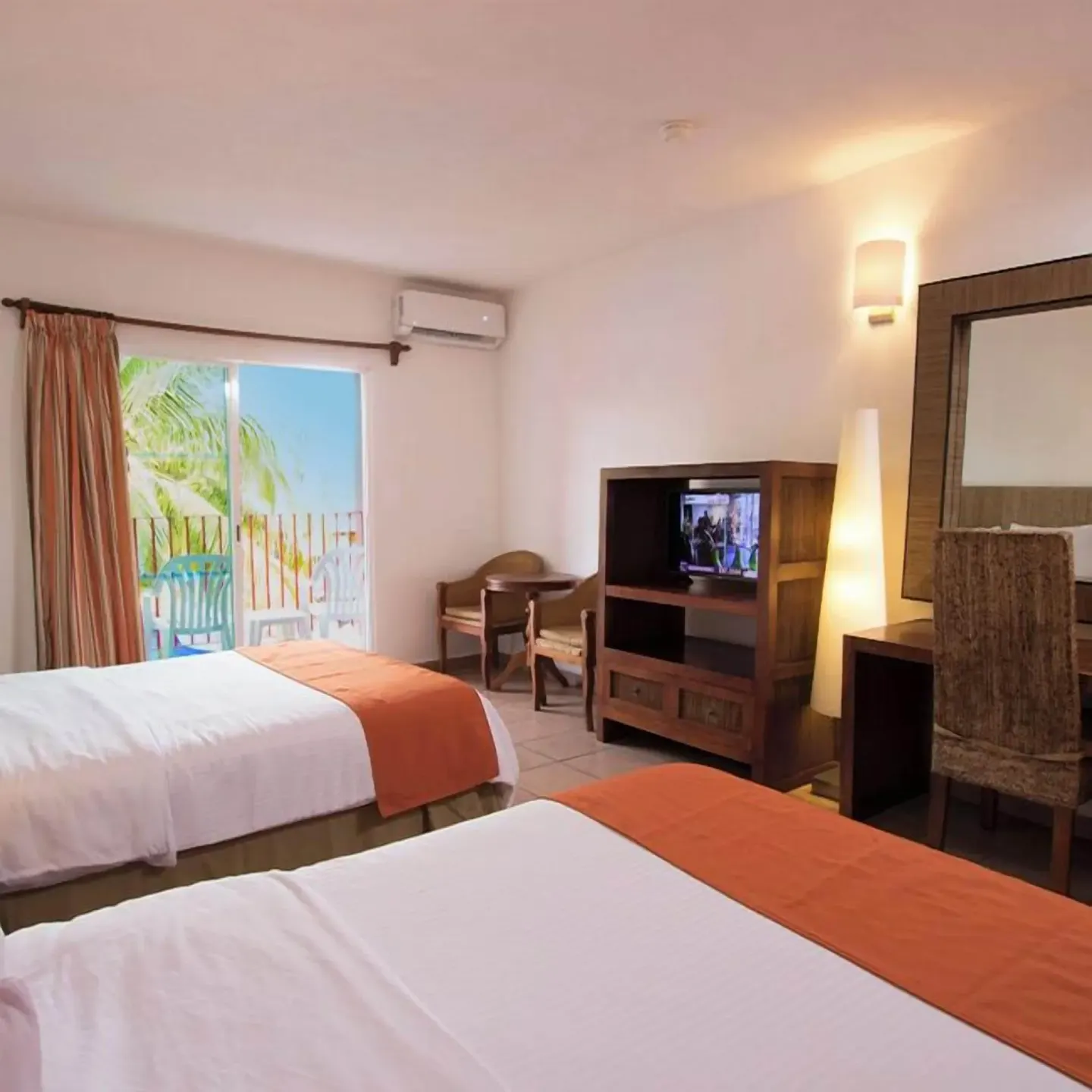 Two-bed guest room with balcony doors and wood TV cabinet at Grand Decameron Complex Bucerias.