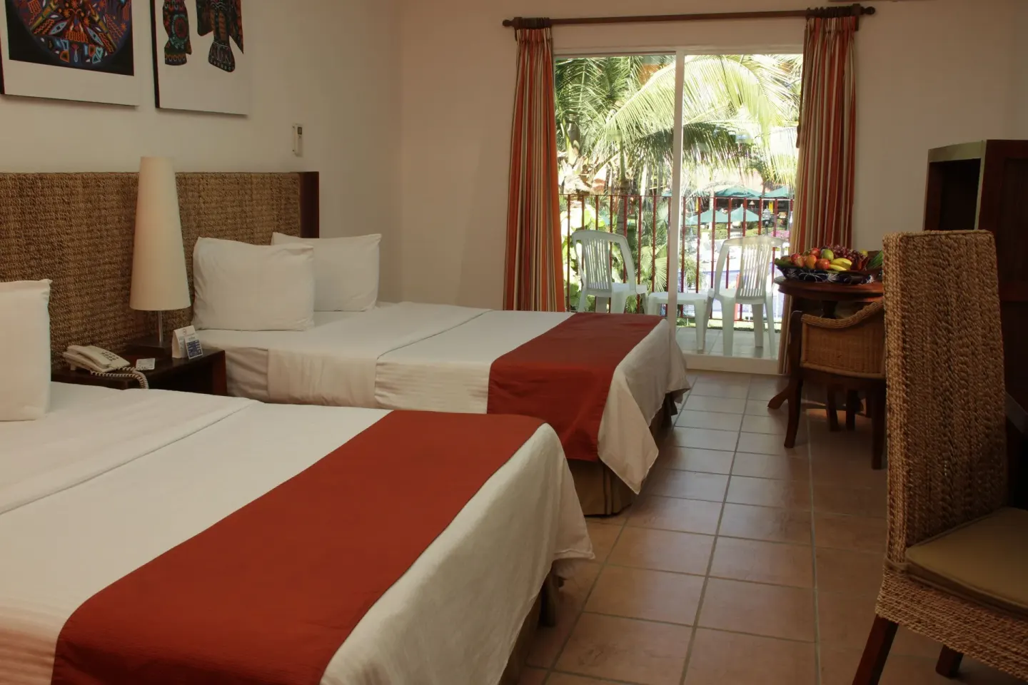 Guest room with two double beds and balcony facing palms at Grand Decameron Complex Bucerias.