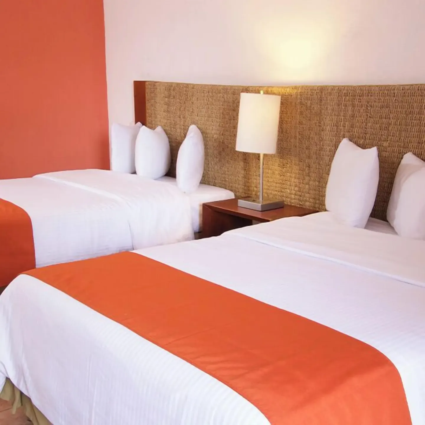 Two double beds with orange runners and woven headboard at Grand Decameron Complex Bucerias.