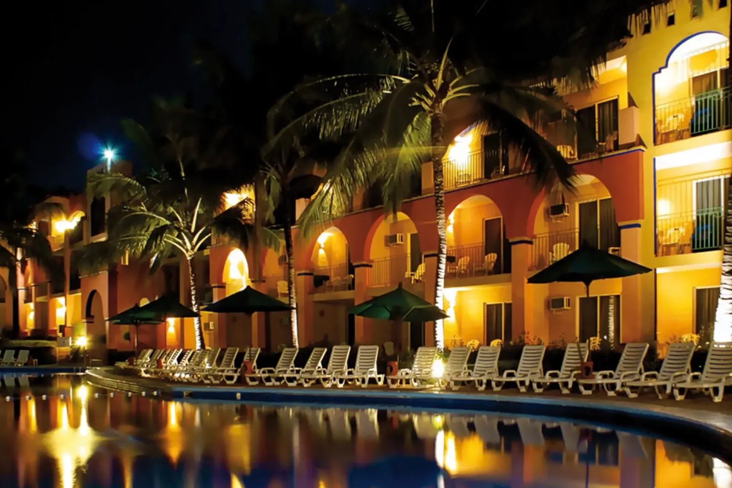 Night view of pool loungers and arched guest buildings at Grand Decameron Complex Bucerias.