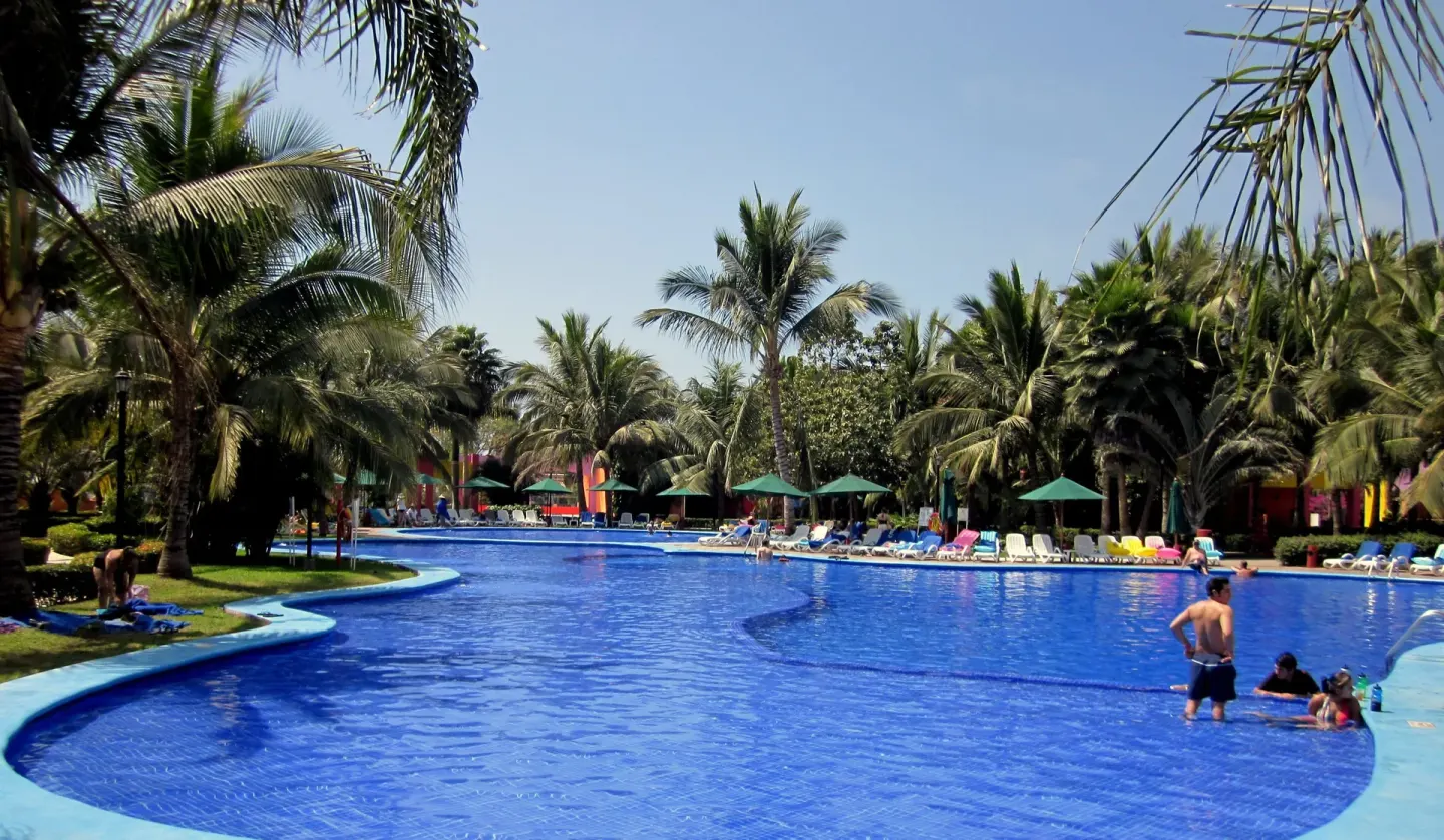 Large palm-lined swimming pool with loungers at Grand Decameron Complex Bucerias.