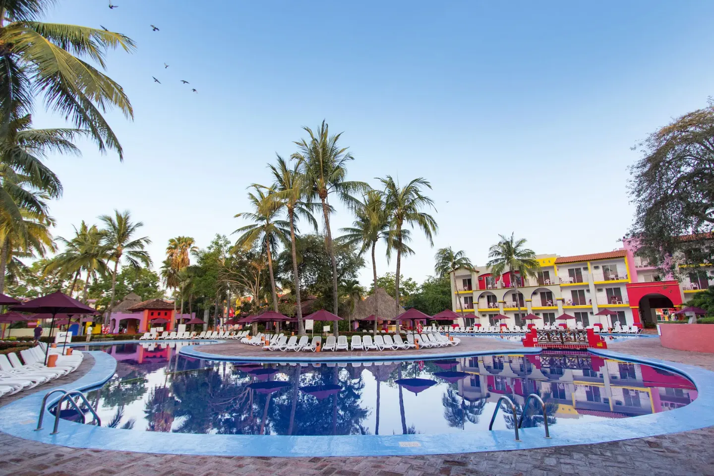 Reflective pool with palms and colorful buildings at Grand Decameron Complex Bucerias.