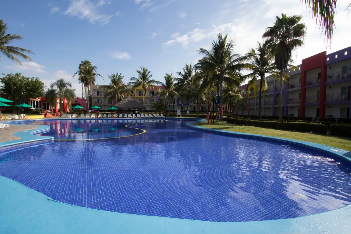 Wide resort pool with palms and colorful buildings at Grand Decameron Complex Bucerias.