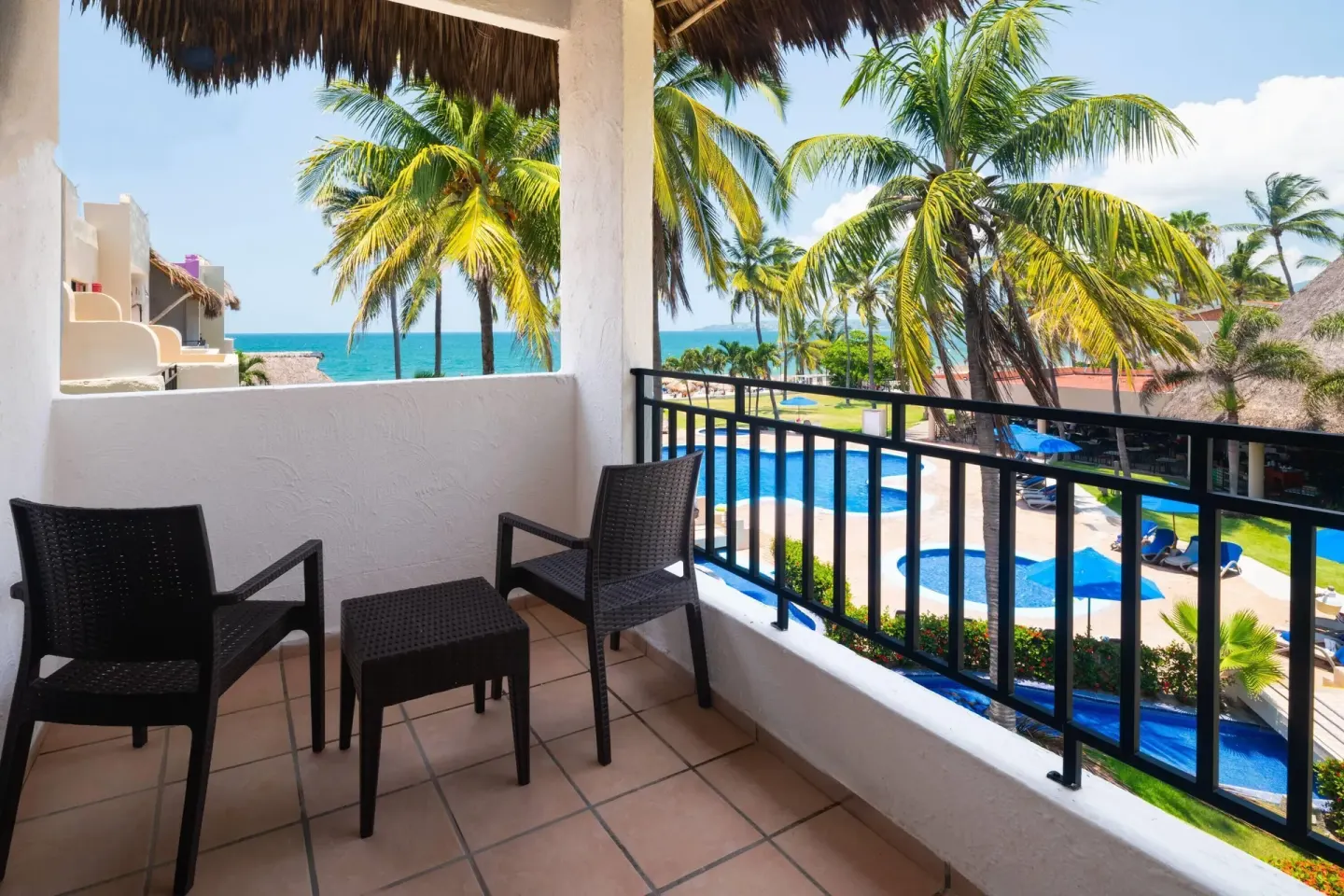 Ocean View balcony with chairs, pool, palms, and sea at Grand Decameron Complex Bucerias.