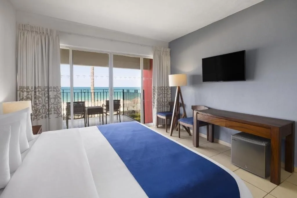 Oceanfront room with king bed, desk, TV, and balcony at Grand Decameron Complex Bucerias.