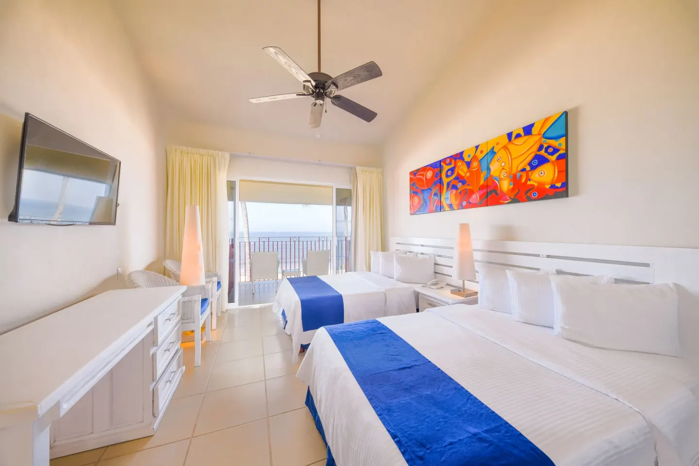 Oceanfront room with two beds, bright artwork, and balcony at Grand Decameron Complex Bucerias.
