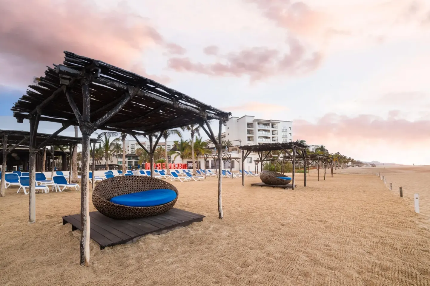 Beach daybeds under wooden shade structures at Grand Decameron Los Cabos.