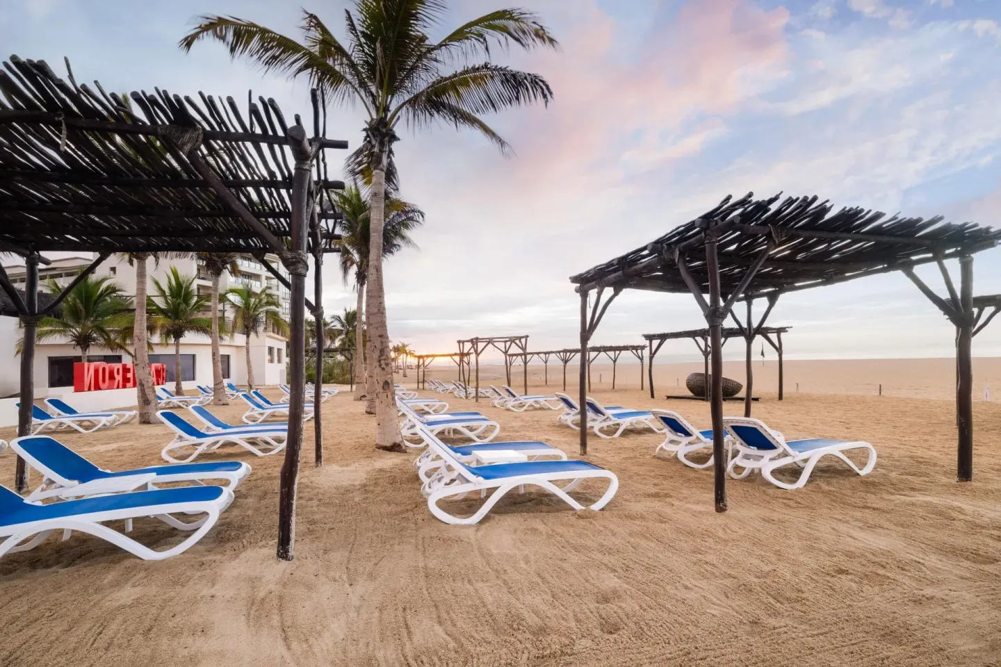 Blue beach loungers and palm trees on the sand at Grand Decameron Los Cabos.