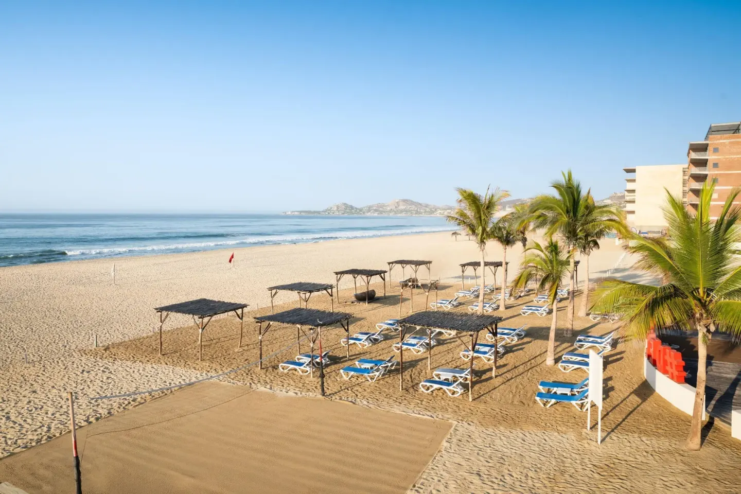 Beach loungers, shade pergolas, palms, and ocean at Grand Decameron Los Cabos.