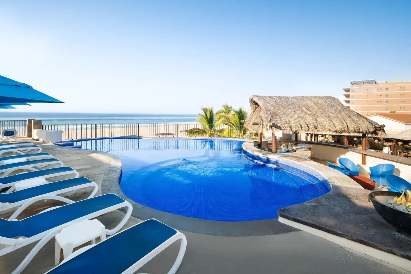 Curved pool, thatched bar, and beach view at Grand Decameron Los Cabos.