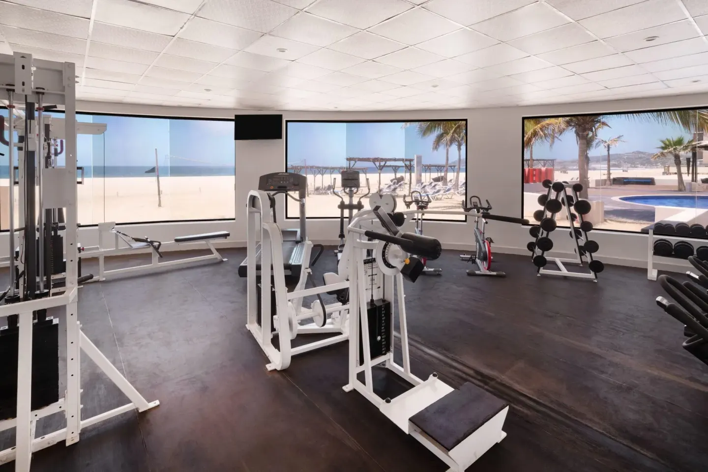Fitness room with weight machines and beach-facing windows at Grand Decameron Los Cabos.