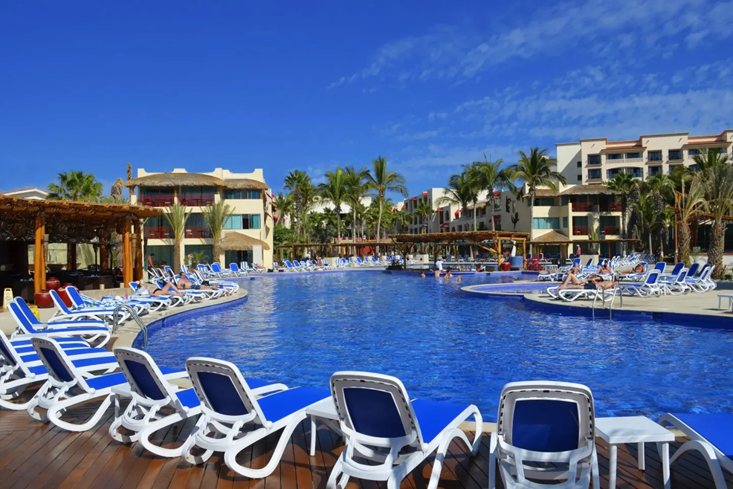 Large resort pool with loungers and guest buildings at Grand Decameron Los Cabos.