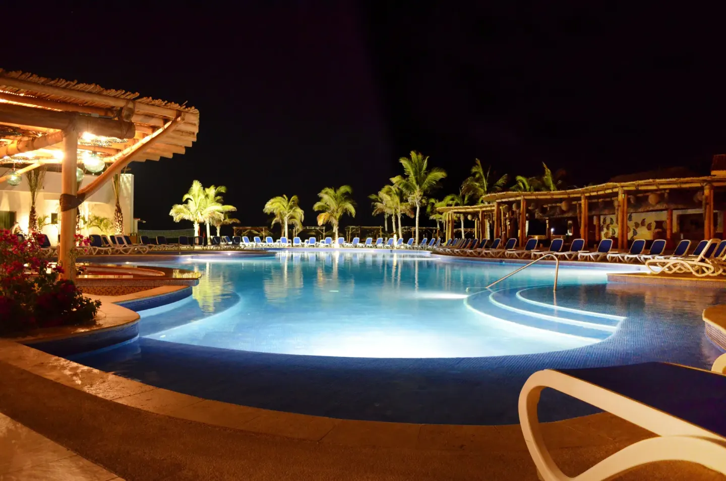 Illuminated pool with loungers and palms at night at Grand Decameron Los Cabos.