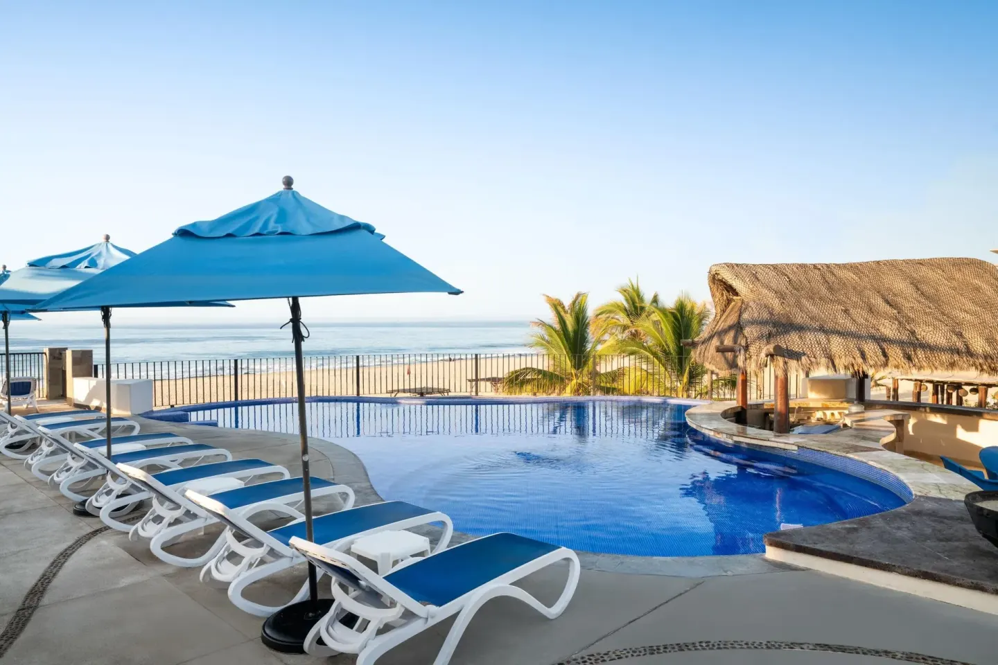 Oceanfront pool with blue loungers and umbrellas at Grand Decameron Los Cabos.