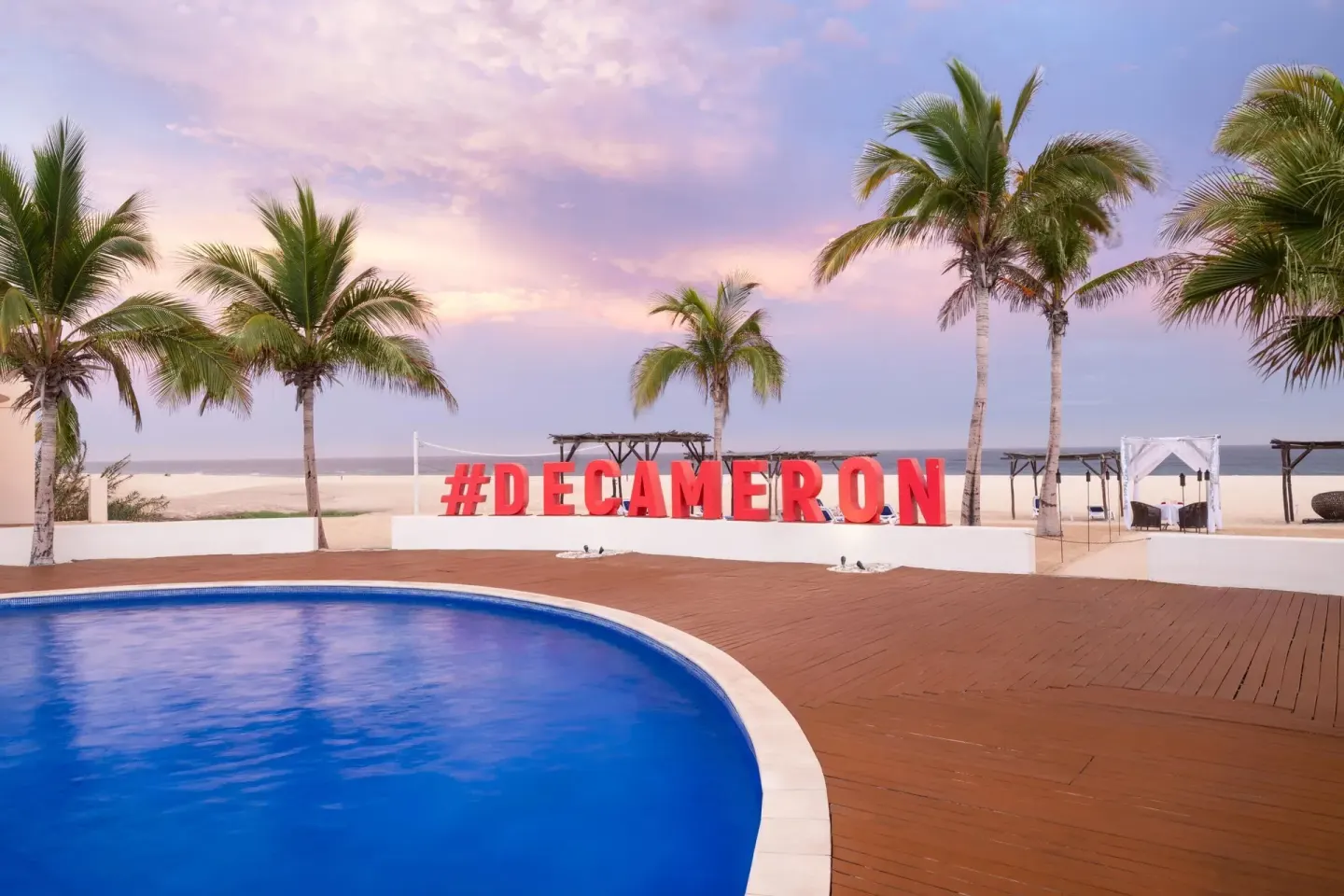 Pool deck with palms and Decameron sign at Grand Decameron Los Cabos.