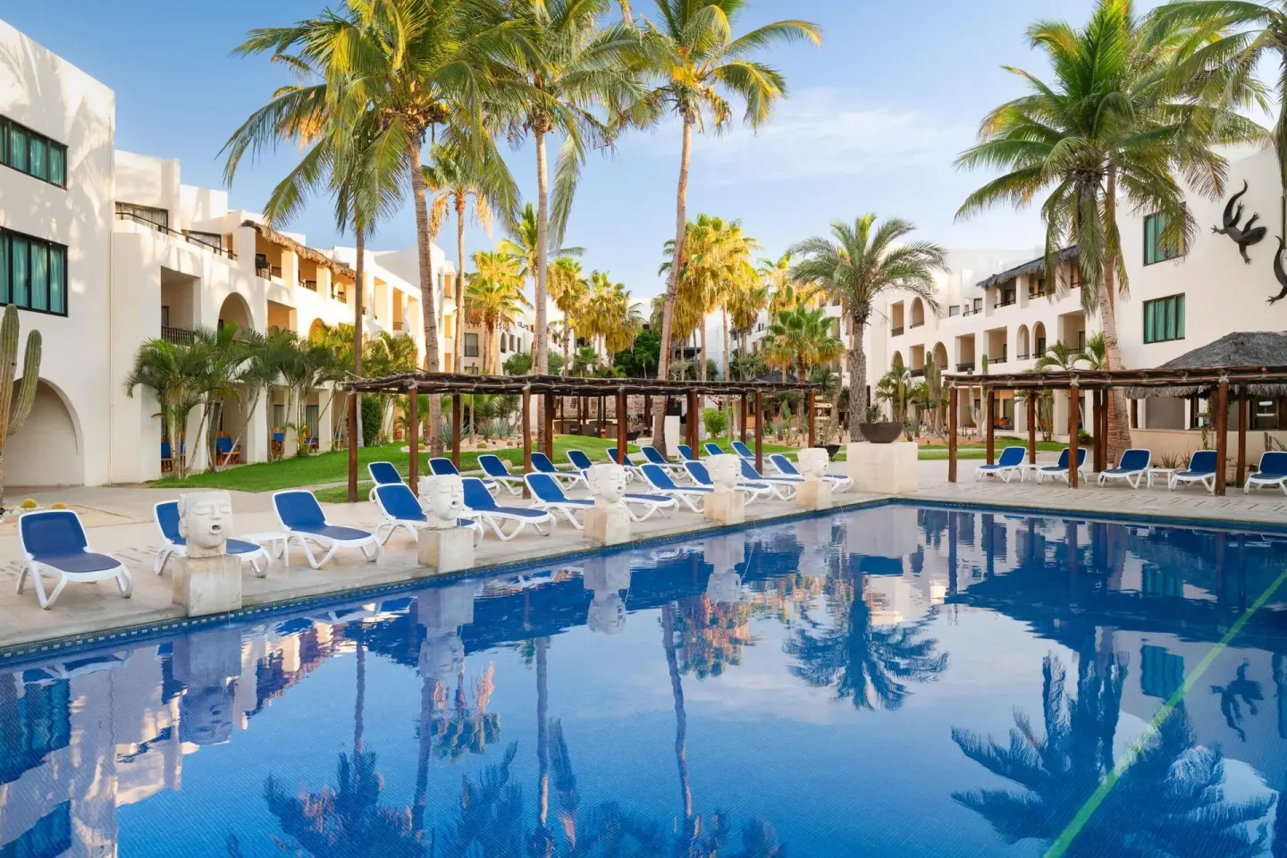 Palm-lined pool courtyard with loungers and white guest buildings at Grand Decameron Los Cabos.