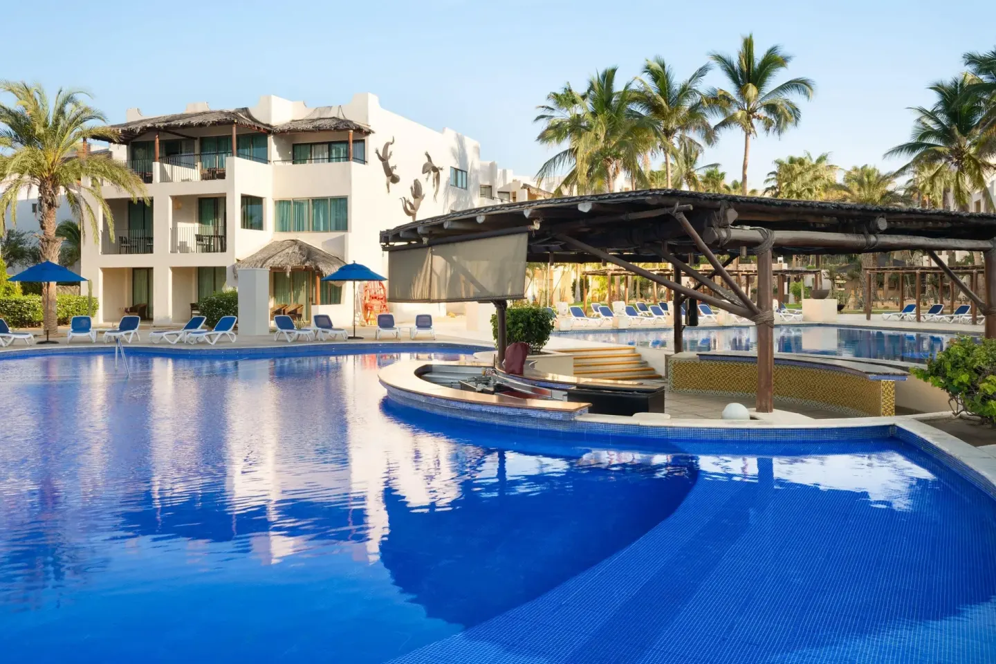 Poolside swim-up bar with blue water and white resort buildings at Grand Decameron Los Cabos.