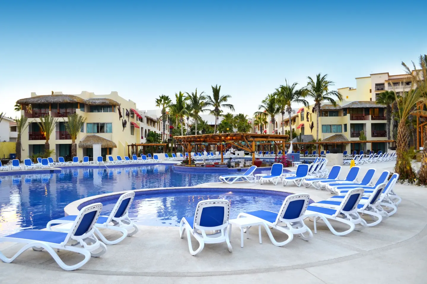 Resort pool with blue loungers and palms at Grand Decameron Los Cabos.