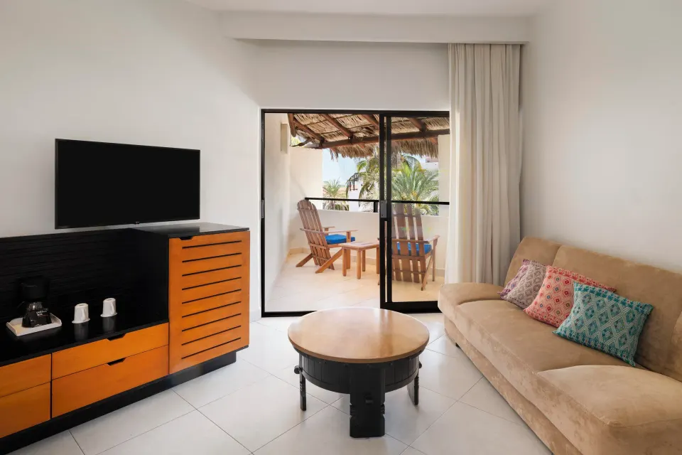 Ocean view room lounge area with sofa and TV at Grand Decameron Los Cabos.