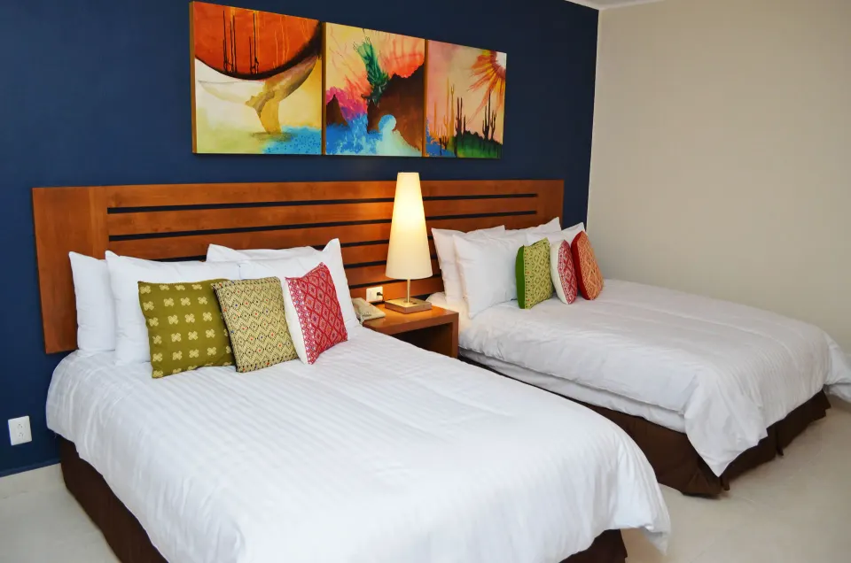 Two-bed ocean view room with colorful pillows at Grand Decameron Los Cabos.